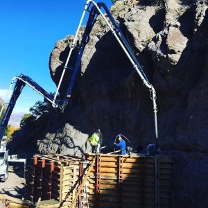 Concrete boom extended over tall foundation walls next to large rock outcropping